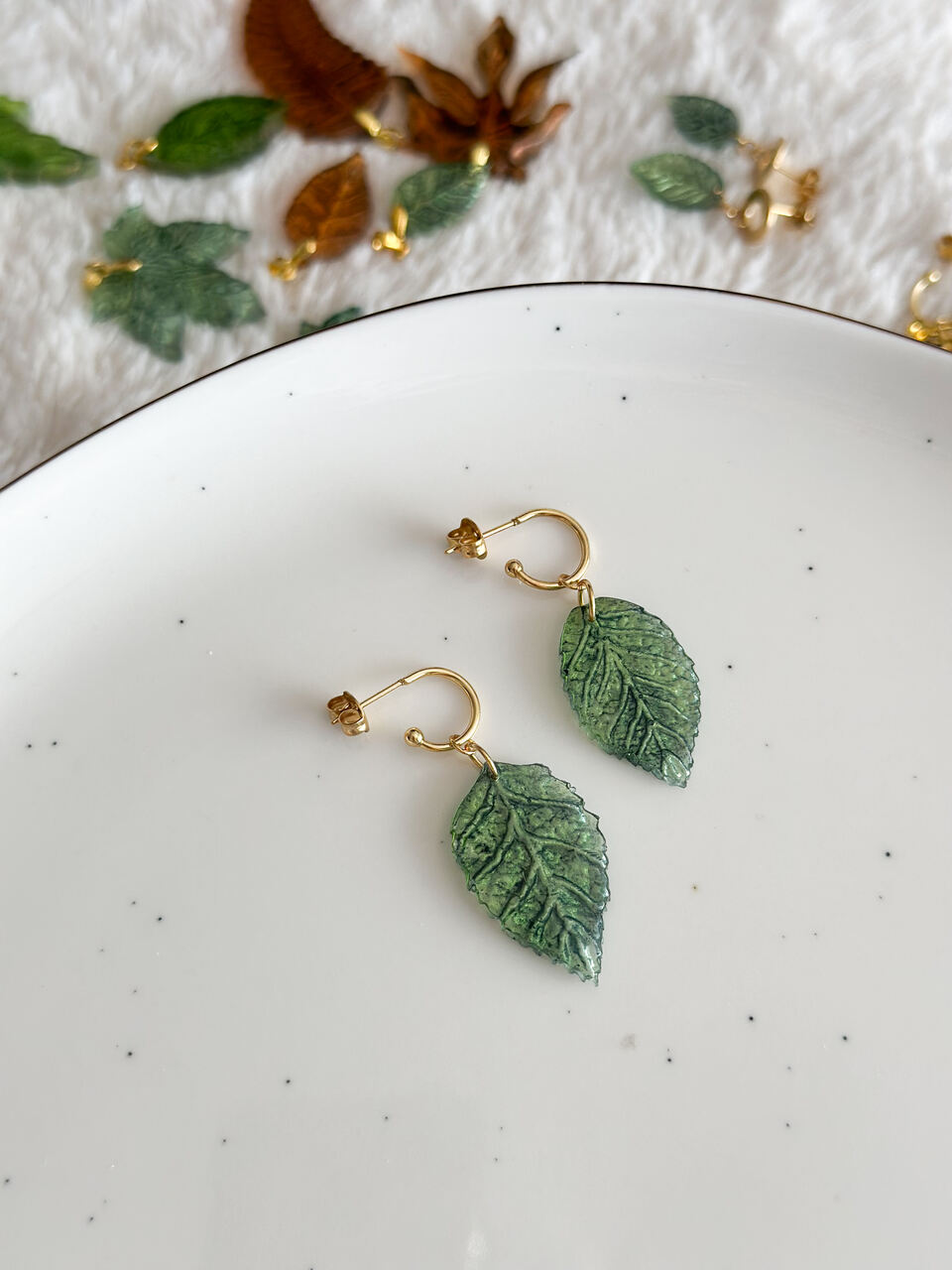 kolczyki zielone liście, ręcznie malowane kolczyki, biżuteria handmade, kolczyki z żywicy, artystyczna biżuteria, kolczyki liście, lekkie kolczyki, kolczyki złote, kolczyki na prezent, unikalna biżuteria, kolczyki dwustronne, kolczyki handmade, kolczyki inspirowane naturą, eleganckie kolczyki, kolczyki z żywicy epoksydowej