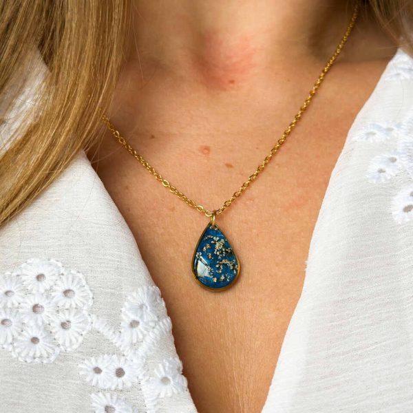 naszyjnik z prawdziwymi kwiatami, naszyjnik z żywicy epoksydowej, biżuteria z suszonymi kwiatami, ręcznie robiony naszyjnik z suszonych kwiatów, biżuteria z kwiatami zalanymi żywicą, kwiaty w żywicy epoksydowej, złoty naszyjnik z żywicy, naszyjnik z kwiatami marchwi zwyczajnej, biżuteria handmade, naszyjnik łezka z żywicy, naszyjnik z niebieskim tłem, elegancki naszyjnik z kwiatami, unikatowa biżuteria z żywicy, pomysł na prezent dla niej, złota biżuteria z kwiatami