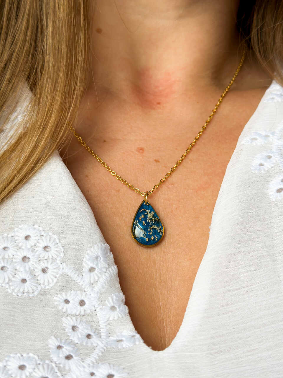 naszyjnik z prawdziwymi kwiatami, naszyjnik z żywicy epoksydowej, biżuteria z suszonymi kwiatami, ręcznie robiony naszyjnik z suszonych kwiatów, biżuteria z kwiatami zalanymi żywicą, kwiaty w żywicy epoksydowej, złoty naszyjnik z żywicy, naszyjnik z kwiatami marchwi zwyczajnej, biżuteria handmade, naszyjnik łezka z żywicy, naszyjnik z niebieskim tłem, elegancki naszyjnik z kwiatami, unikatowa biżuteria z żywicy, pomysł na prezent dla niej, złota biżuteria z kwiatami