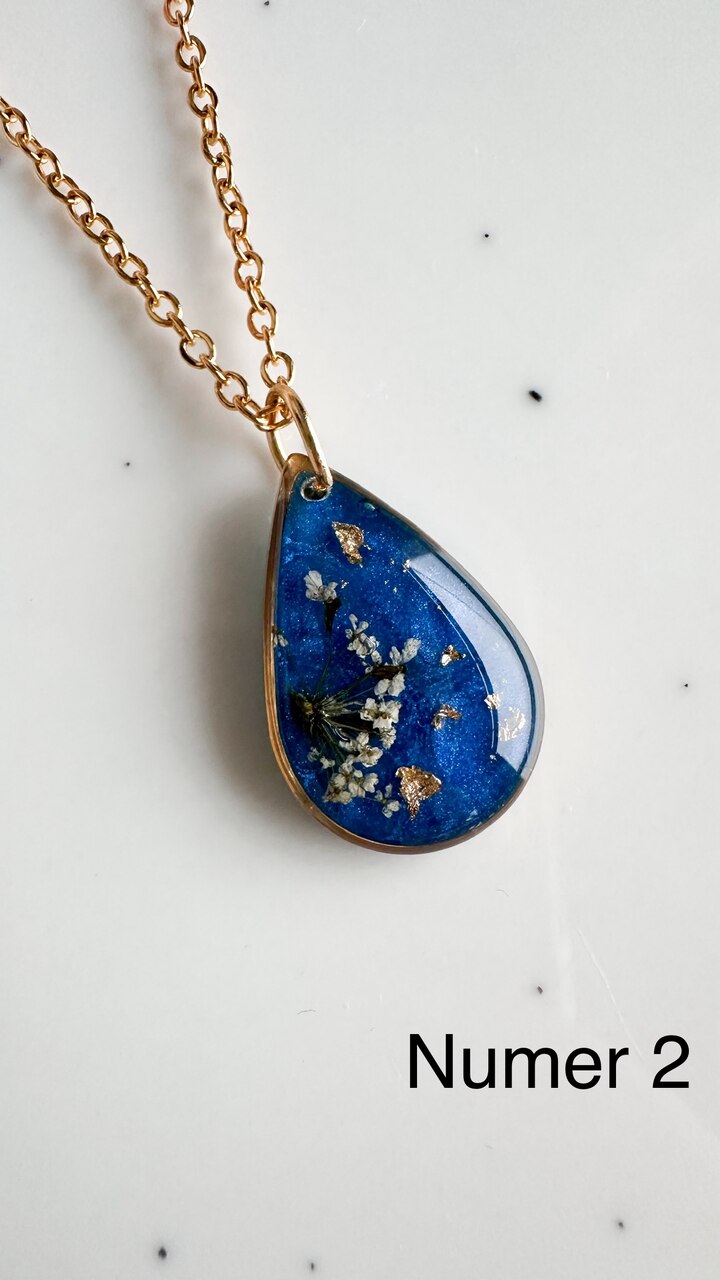 naszyjnik z prawdziwymi kwiatami, naszyjnik z żywicy epoksydowej, biżuteria z suszonymi kwiatami, ręcznie robiony naszyjnik z suszonych kwiatów, biżuteria z kwiatami zalanymi żywicą, kwiaty w żywicy epoksydowej, złoty naszyjnik z żywicy, naszyjnik z kwiatami marchwi zwyczajnej, biżuteria handmade, naszyjnik łezka z żywicy, naszyjnik z niebieskim tłem, elegancki naszyjnik z kwiatami, unikatowa biżuteria z żywicy, pomysł na prezent dla niej, złota biżuteria z kwiatami