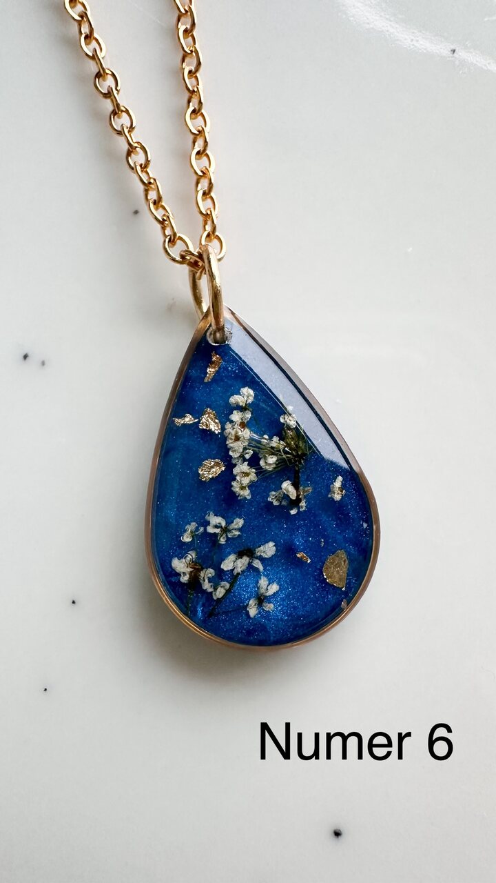 naszyjnik z prawdziwymi kwiatami, naszyjnik z żywicy epoksydowej, biżuteria z suszonymi kwiatami, ręcznie robiony naszyjnik z suszonych kwiatów, biżuteria z kwiatami zalanymi żywicą, kwiaty w żywicy epoksydowej, złoty naszyjnik z żywicy, naszyjnik z kwiatami marchwi zwyczajnej, biżuteria handmade, naszyjnik łezka z żywicy, naszyjnik z niebieskim tłem, elegancki naszyjnik z kwiatami, unikatowa biżuteria z żywicy, pomysł na prezent dla niej, złota biżuteria z kwiatami