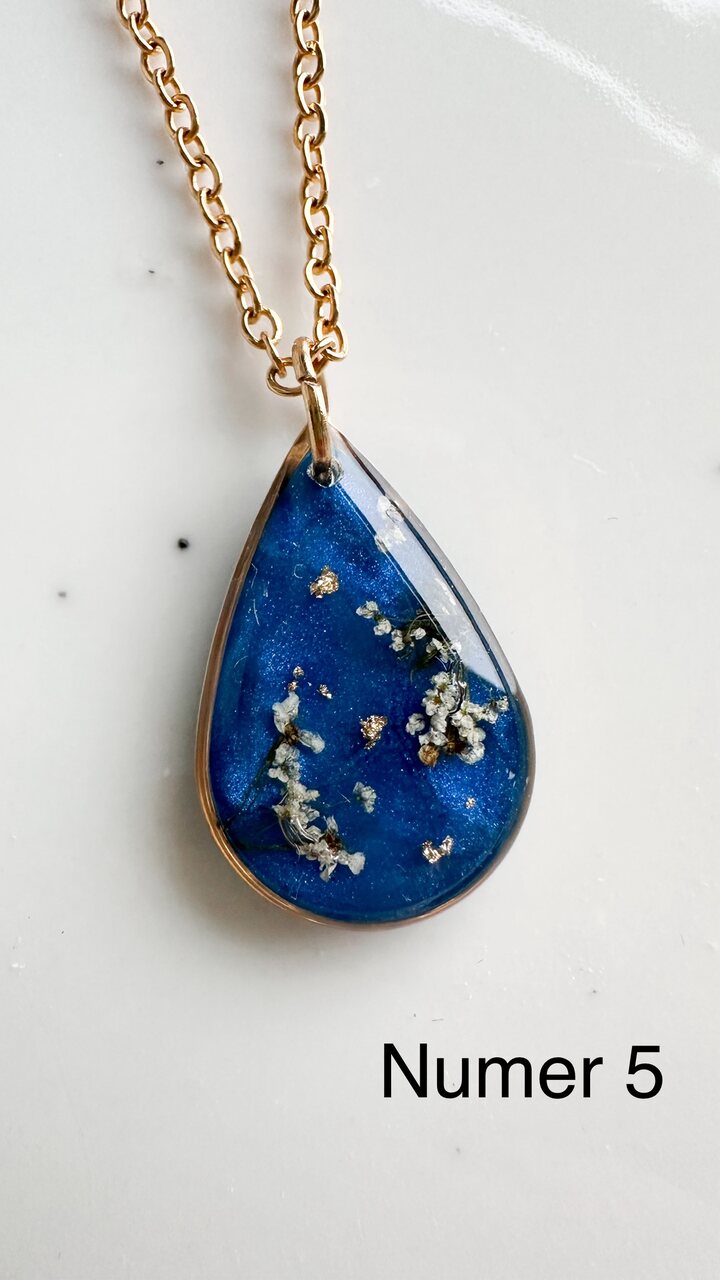 naszyjnik z prawdziwymi kwiatami, naszyjnik z żywicy epoksydowej, biżuteria z suszonymi kwiatami, ręcznie robiony naszyjnik z suszonych kwiatów, biżuteria z kwiatami zalanymi żywicą, kwiaty w żywicy epoksydowej, złoty naszyjnik z żywicy, naszyjnik z kwiatami marchwi zwyczajnej, biżuteria handmade, naszyjnik łezka z żywicy, naszyjnik z niebieskim tłem, elegancki naszyjnik z kwiatami, unikatowa biżuteria z żywicy, pomysł na prezent dla niej, złota biżuteria z kwiatami