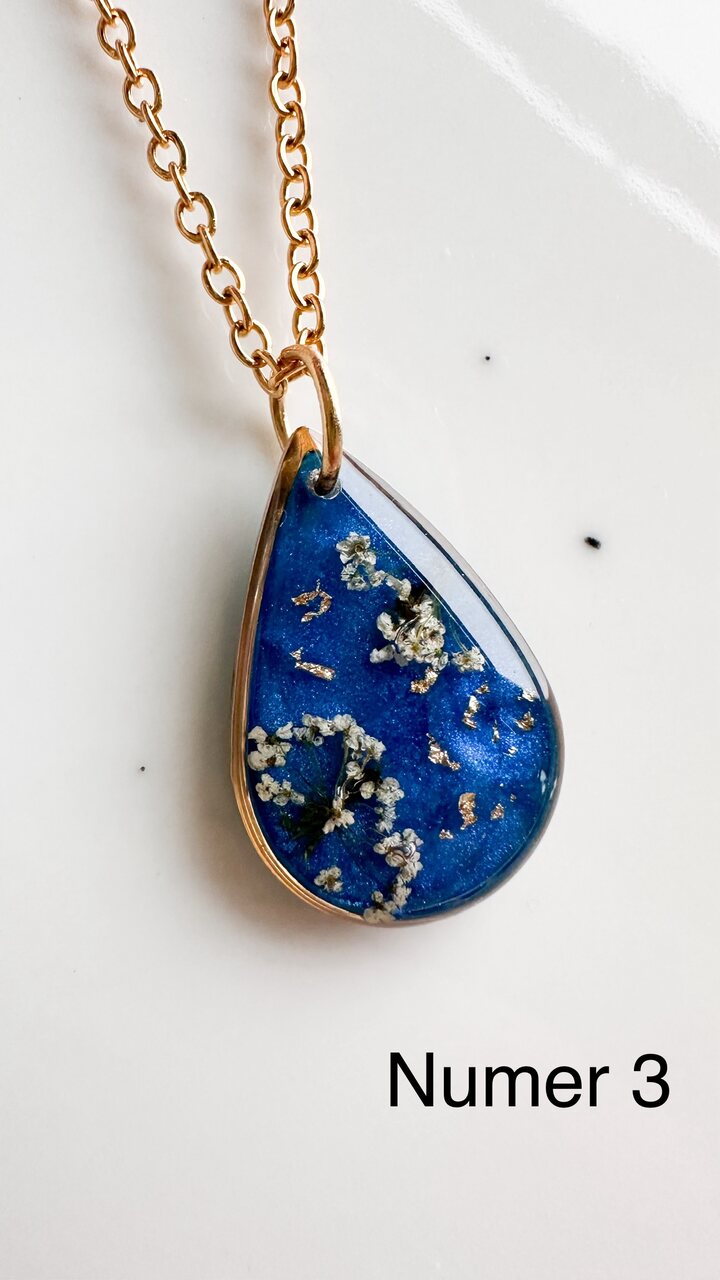 naszyjnik z prawdziwymi kwiatami, naszyjnik z żywicy epoksydowej, biżuteria z suszonymi kwiatami, ręcznie robiony naszyjnik z suszonych kwiatów, biżuteria z kwiatami zalanymi żywicą, kwiaty w żywicy epoksydowej, złoty naszyjnik z żywicy, naszyjnik z kwiatami marchwi zwyczajnej, biżuteria handmade, naszyjnik łezka z żywicy, naszyjnik z niebieskim tłem, elegancki naszyjnik z kwiatami, unikatowa biżuteria z żywicy, pomysł na prezent dla niej, złota biżuteria z kwiatami