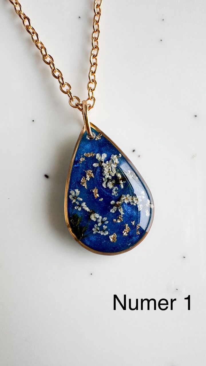 naszyjnik z prawdziwymi kwiatami, naszyjnik z żywicy epoksydowej, biżuteria z suszonymi kwiatami, ręcznie robiony naszyjnik z suszonych kwiatów, biżuteria z kwiatami zalanymi żywicą, kwiaty w żywicy epoksydowej, złoty naszyjnik z żywicy, naszyjnik z kwiatami marchwi zwyczajnej, biżuteria handmade, naszyjnik łezka z żywicy, naszyjnik z niebieskim tłem, elegancki naszyjnik z kwiatami, unikatowa biżuteria z żywicy, pomysł na prezent dla niej, złota biżuteria z kwiatami