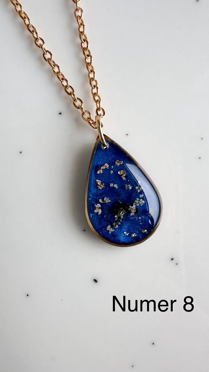 naszyjnik z prawdziwymi kwiatami, naszyjnik z żywicy epoksydowej, biżuteria z suszonymi kwiatami, ręcznie robiony naszyjnik z suszonych kwiatów, biżuteria z kwiatami zalanymi żywicą, kwiaty w żywicy epoksydowej, złoty naszyjnik z żywicy, naszyjnik z kwiatami marchwi zwyczajnej, biżuteria handmade, naszyjnik łezka z żywicy, naszyjnik z niebieskim tłem, elegancki naszyjnik z kwiatami, unikatowa biżuteria z żywicy, pomysł na prezent dla niej, złota biżuteria z kwiatami