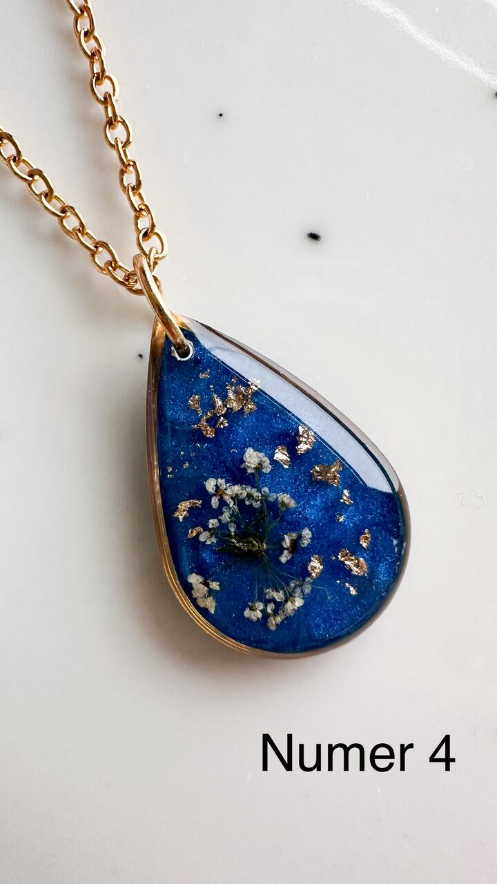 naszyjnik z prawdziwymi kwiatami, naszyjnik z żywicy epoksydowej, biżuteria z suszonymi kwiatami, ręcznie robiony naszyjnik z suszonych kwiatów, biżuteria z kwiatami zalanymi żywicą, kwiaty w żywicy epoksydowej, złoty naszyjnik z żywicy, naszyjnik z kwiatami marchwi zwyczajnej, biżuteria handmade, naszyjnik łezka z żywicy, naszyjnik z niebieskim tłem, elegancki naszyjnik z kwiatami, unikatowa biżuteria z żywicy, pomysł na prezent dla niej, złota biżuteria z kwiatami