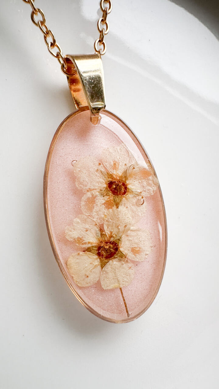 naszyjnik z kwiatów zalanych żywicą, biżuteria z prawdziwych kwiatów, biżuteria z suszonych kwiatów, ręcznie robiona biżuteria z żywicy, złoty naszyjnik elipsa, złoty medalion z kwiatem, biżuteria handmade, naszyjnik z żywicy z kwiatami, biżuteria artystyczna, biżuteria z natury, biżuteria z żywicy epoksydowej, delikatna biżuteria dla niej, oryginalny pomysł na prezent dla niej, unikalny prezent dla kobiety, naszyjnik z prawdziwymi kwiatami, biżuteria z żywicy handmade, kwiaty zatopione w żywicy, biżuteria dla miłośniczki natury